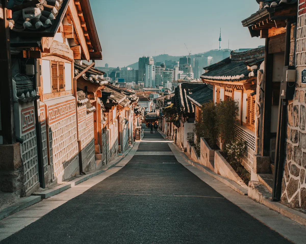 Rua de Bukchon Hanok Village, em Seul, com casas tradicionais coreanas e a cidade ao fundo.